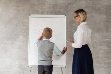 A cute teacher in white blouse and blue skirt watching her pupil drawing geometry figure on desk