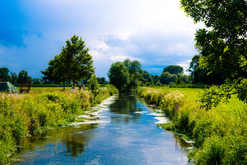 View on long river on a sunny summer day with dark storm clouds