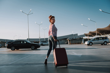 Charming young woman with travel suitcase standing in airport