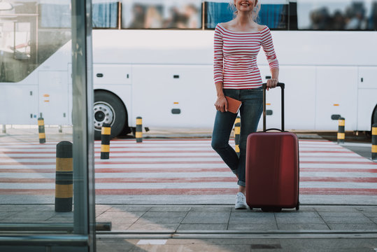 Joyful young woman with travel luggage bag standing in airport