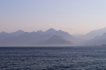 Naklejka na ściany i meble Mountains in a blue haze and sunset over the sea