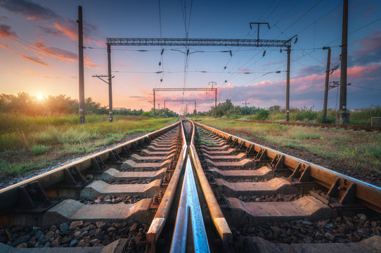 Railway station and beautiful sky at sunset. Summer rural industrial landscape with railroad, blue sky with colorful clouds and sunlight, green grass. Railway platform. Transportation. Heavy industry