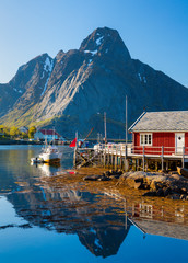 Reine Village on the Lofoten Islands,  Norway. The Typical Norwegian fishing village of Reine under midnight sun,  with the typical rorbu houses.  Mountain In Background - obrazy, fototapety, plakaty