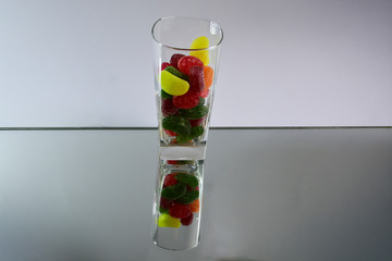 Multicolored tasty candies in a glass cup on the mirror. The reflection of the glass and sweets creates a striking effect of volume and increases the number of objects in the frame, which makes sweets