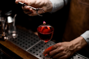 Professional bartender putting a little rose bud to the red cocktail in the glass