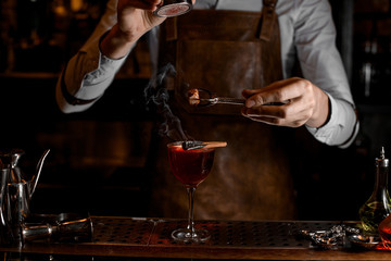 Bartender add spices for a decor above a delicious red cocktail in the glass