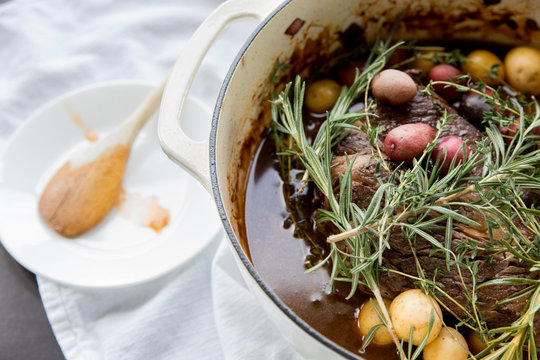  A Close-up View Of A Roast Beef Dinner With Vegetables And Herbs In A Dutch Oven Cooking Pot