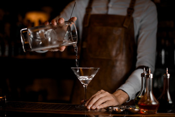 Professional bartender pouring an alcoholic drink from the measuring cup to the martini glass