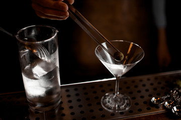 Professional male bartender putting an olive with tweezers to the martini glass