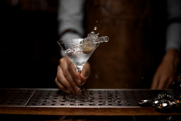 Professional bartender mixing a transparent alcoholic drink in the martini glass with one olive