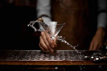 Male bartender mixing a transparent alcoholic drink in the martini glass with one olive