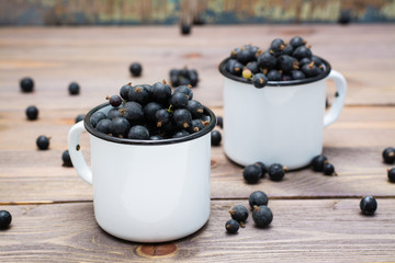 Ripe black currants in metal white mugs on a wooden table
