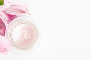 Face cream in white jar on a white background with pink flowers. Concept natural cosmetics, organic beauty, flower arrangement. Copy space, top view, flat lay.
