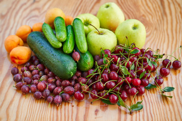 Seasonal fruits and vegetables harvested in home garden on wooden table consist from red gooseberries, sour cherries, apples, apricots and cucumbers. Full of nutrients and vitamins for vegan raw diet