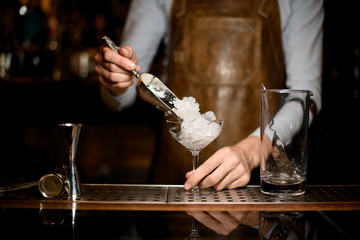 Professional male bartender putting crushed ice to the glass