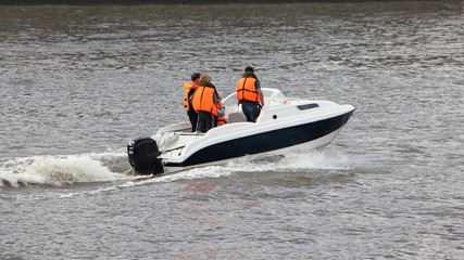 White plastic cabin motor boat with passengers in orange life jackets quickly floats on the river...