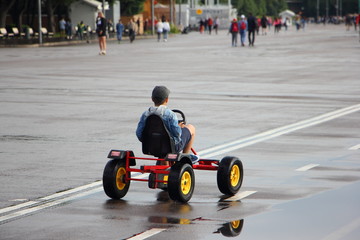 Little boy rides a pedal quadro bike on a wet road with markings, outdoor activities in the summer Park after rain