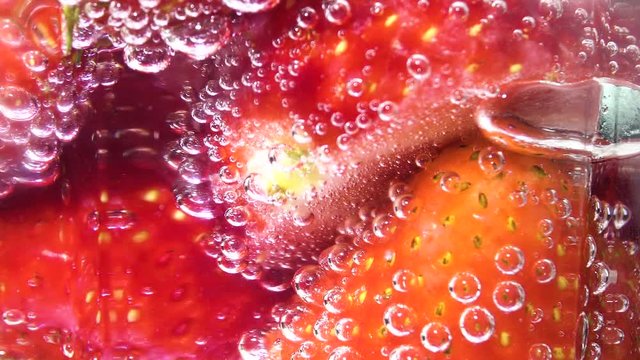 Glass soda water with ice cubes and strawberries, centre screen. Fizzy bubbles rising. Rotating background.