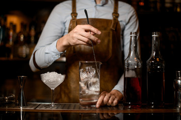 Male bartender stirring an alcoholic drink with ice in the measuring glass cup
