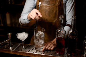 Bartender stirring an alcoholic drink with ice in the measuring glass cup