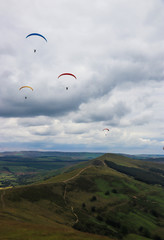 Group of paragliders flying above valley with green mountain and clouds in the background