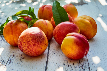 Naklejka na ściany i meble Ripe peaches with leaves on the old wooden table against the background of green leaves in the garden. Soft selective focus