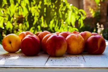 Ripe peaches with leaves on the old wooden table against the background of green leaves in the garden. Soft selective focus