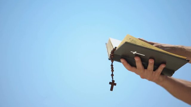 Hands holding bible and rosary on blue background, praying to god, template