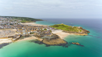 Aerial view of picturesque seaside town of St Ives with sandy beaches by turquoise sea, small fishing port, fortified headland,  in Cornwall , south east England on a cloudy summer day .