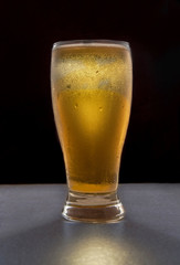 Cold beer in a glass, in a dark background as part of low key light photography or dark food photography