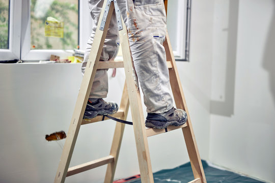 Worker Standing On The Ladder And Renovating House.