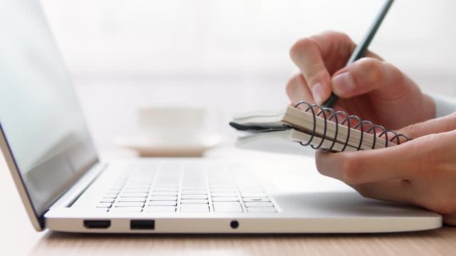Woman freelancer working on laptop at home-office. Close up of female hands with notepad. Businesswoman writing in planner at work. Camera trucking