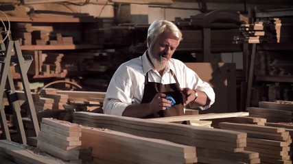 Old male’s Carpenter’s hands are holding a ruler and a pencil. Carpenter measures the line of wood and make a pencil mark. He’s working Handmade in big Bright Workshop.Wood Carver. Furniture Factory.