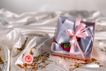 Beautiful gift with a bow on a beige satin fabric. Gift on flowers background