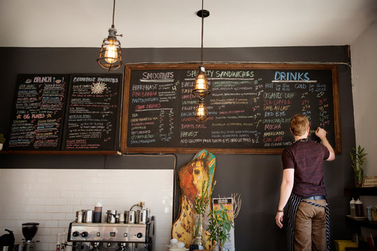 Rear view of waiter writing menu on blackboard in cafe