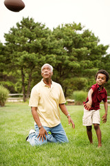 Naklejka premium Boy with his grandfather throwing American football outdoors