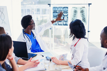 Multiracial team of young doctors discussing computed tomography result in the clinic. Showing...