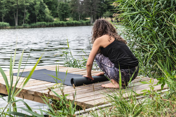 Kobieta stojąca na molo zwija matę do ćwiczeń. Poranna joga nad brzegiem jeziora.