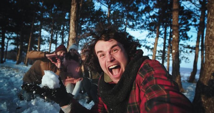 In front of the camera charismatic guy with curly hair and his friends make a funny video very excited in the middle of snowy forest