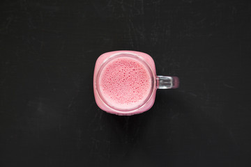 Glass jar mug filled with raspberry smoothie on a black background, top view. From above, flat lay,...