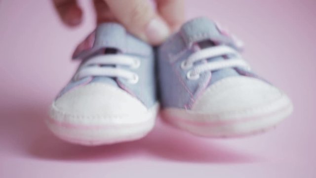 Children's denim sports shoes for girls, on a pink background closeup. mom hand depicts dance baby booties the concept of children's clothing or pregnancy