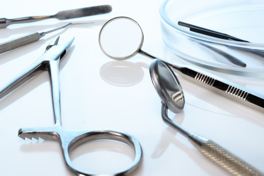 Dentist equipment: dental mirrors, spatula, kornzange or forceps, dental burs in Petri dish. Dental tools on blue glossy surface, closeup.