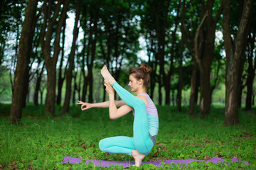 Thin brunette girl plays sports and performs beautiful and sophisticated yoga poses in a summer...