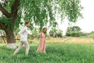 Obraz premium Young loving couple having fun and running on the green grass on the lawn with their beloved domestic dog breed Beagle and a bouquet of wildflowers