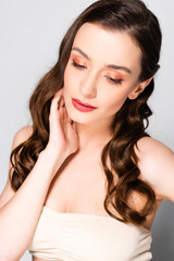 Fototapeta premium beautiful brunette woman with curls and makeup looking down isolated on grey