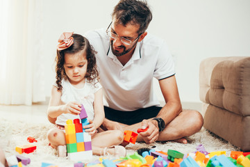 Father and daughter playing together with block toys in living room
