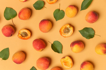 Apricots on an orange background, the flat lay image of ripe apricots and leaves