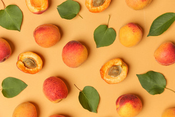 Apricots on an orange background, the flat lay image of ripe apricots and leaves