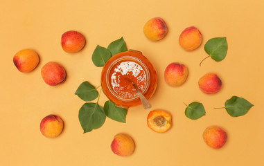 Jar of apricots jam and fresh apricots on an orange background, top view
