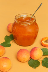 Jar of apricots jam and fresh apricots on an orange background